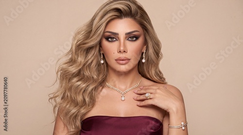 Elegant beautiful woman wearing a luxury diamond and pearl jewelry set including a V shaped collar necklace, drop earrings and matching bracelet on a beige background