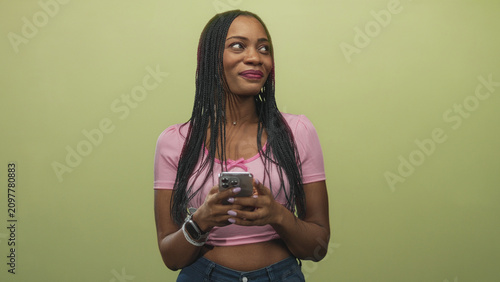 Konstfotografi African woman holding smartphone with both hands, smiling and glancing sideways in a studio; confidence ease