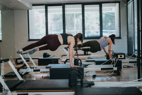 Foto Two women perform advanced pilates exercises on reformer machines in a bright studio