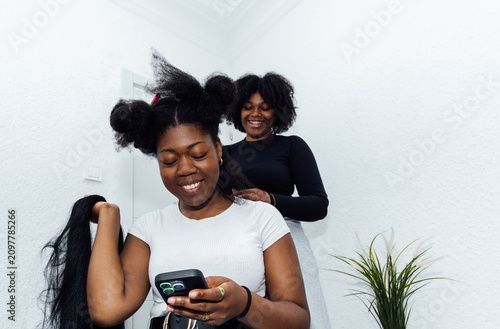Young woman getting afro hair braided by friend