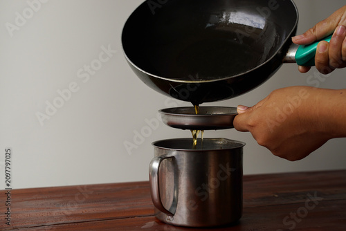 Fotografi Close-up of hands straining used cooking oil into a stainless steel container