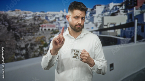 Fotografie Man holding coffee mug that reads i am the boss, pointing finger with right hand in studio set, white shirt and beard; irony leadership