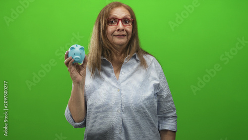 фотографія Woman holds blue piggy bank in left hand and makes a v sign near nose while facing camera in studio; playful saving