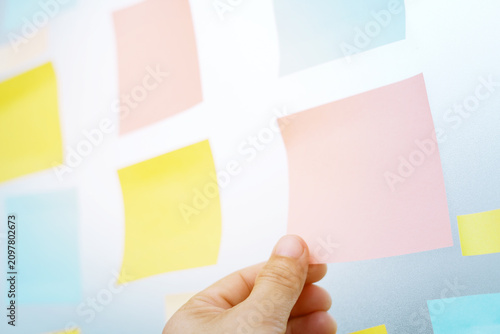 close up hand people business man post it notes in the wall at meeting room. Sticky note paper reminder schedule board. Colorful variety copy empty space. soft focus.