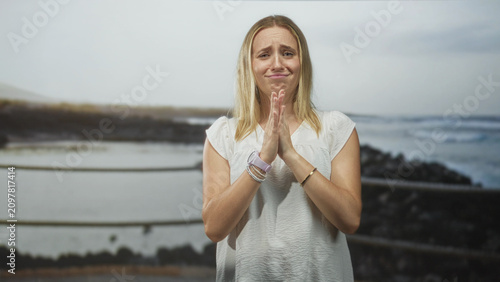 Fotografie Woman pinches fingers in a money gesture with both hands, wearing a white blouse and watch in studio; pleading request