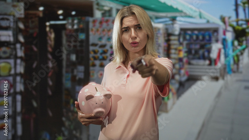 Картината върху платно Woman holding pink piggy bank, points finger toward camera on street; financial responsibility determination