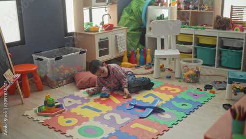 Принти на полотні Boy kneeling and crawling while playing with a toy airplane and stacking blocks on a colorful foam number mat in a playroom building; playful imagination