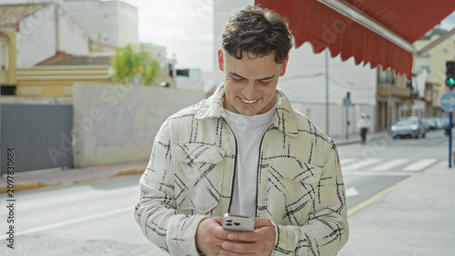 Fotografie Man holding smartphone looks down at screen on a city street under a red awning; calm concentration