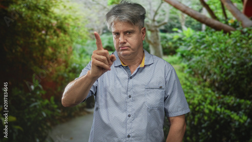 Fényképezés Man pointing index finger forward on a forest path, visible forearm and stern expression; disapproval caution