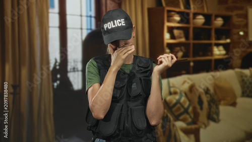 Canvastavla Blonde woman police covering mouth with hand while holding a radio inside building, wearing cap and vest; amusement