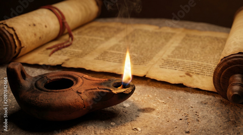 Clay oil lamp burning on stone table with open scroll of Isaiah in soft light