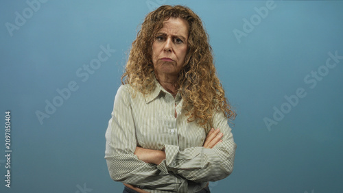 Canvas Print Woman with crossed arms and visible hands frowning in a studio portrait with blue backdrop; displeasure sternness