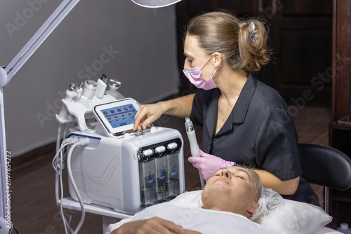 Obraz na plátně Cosmetic physician prepares a professional hydradermabrasion facial treatment by adjusting a multifunction skincare device before performing a noninvasive cosmetic procedure