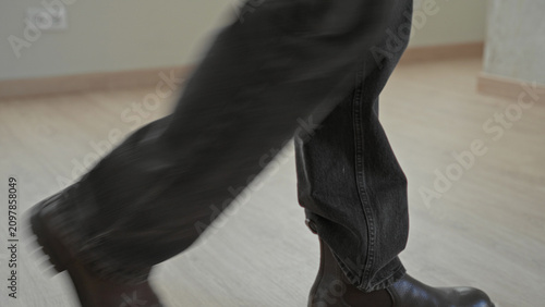 Fotografie Man walking in leather boots and jeans, stride visible on laminate floor across an empty room inside a building; quiet determination