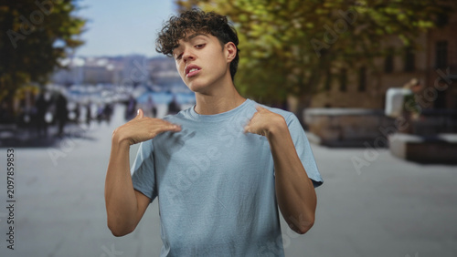Foto Teenage man touches neck and flicks hands toward chest on pedestrian street by the waterfront; confidence youth attitude