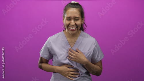 фотографія Woman laughing with hand over mouth and hands clasped on stomach in a purple studio; joy playfulness warmth