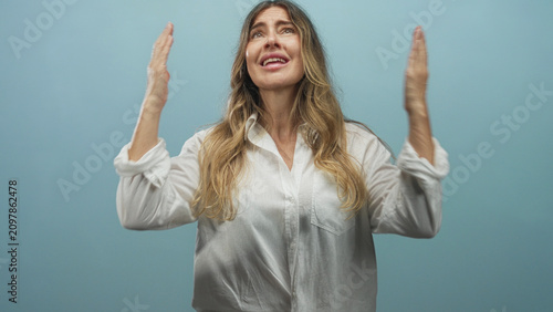 Konstfotografi Woman raises hands with palms open and looks upward in a blue studio, eyes closed in a pleading gesture; plea desperation