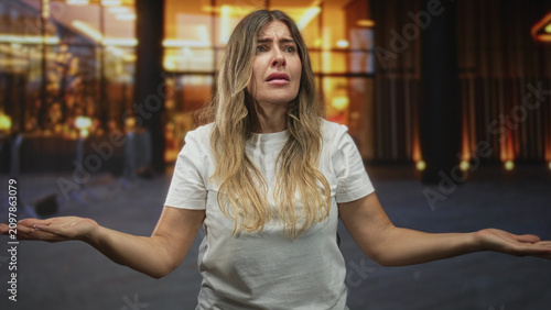 Foto Woman raising hands with open mouth reaching forward, visible hands and forearms, standing in a building near stanchions and warm lights; pleading hope