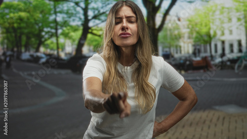 Fotografie Woman pointing finger at camera on street with hands on hips and stern expression, middle age hispanic adult; defiance assertiveness