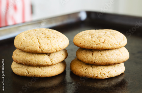 Freshly baked homemade peanut butter cookies stacked on a metal baking sheet with a soft kitchen background.