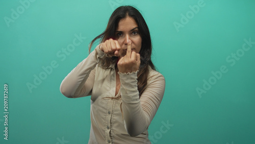 Fotografía Woman showing middle finger and clenched fist in studio with teal background and intense stare; defiance