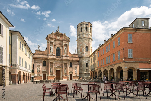 Piazza San Prospero in Reggio Emilia Italy, featuring the baroque facade of the Basilica of San Prospero and its famous octagonal bell tower. The square is depicted with outdoor cafe tables and chairs