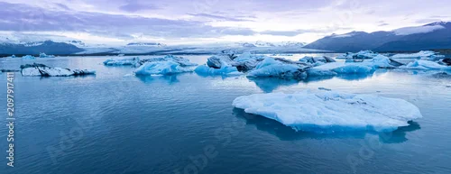 Panel kuchenny z motywem Panoramic view of Jökulsárlón Glacier Lagoon in southeast Iceland, where floating blue icebergs drift across calm waters beneath Vatnajökull Glacier and rugged mountain peaks.