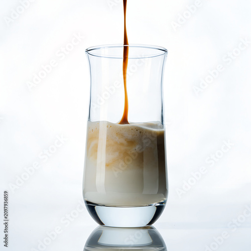 High-key studio photograph of a transparent coffee glass perfectly centered on a white reflective surface, espresso descending smoothly into milk, producing soft beige gradients. Bright clean lighting