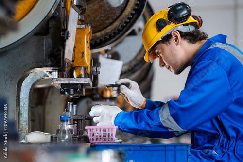 Skilled industrial technician in safety gear using tool for checking and maintenance heavy metal press machinery for quality control in modern manufacturing factory production line.