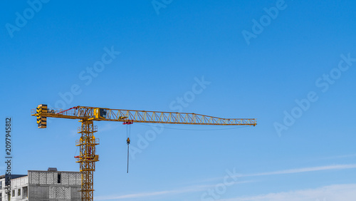 Fotografija Photo of the construction of multi-storey building with a monolithic frame and walls erected with masonry from cellular foam blocks using an orange tower crane against blue background sky