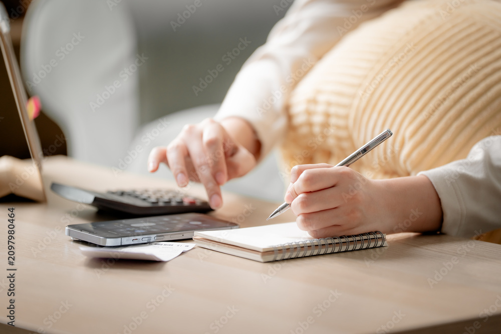 Fototapeta premium Personal budgeting concept. Anonymous person calculating household expenses with calculator while writing notes beside smartphone at home. Budget, finance, savings, planning, expenses