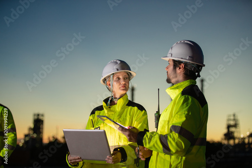 Engineers discussing construction plans at dusk with safety gear and equipment in industrial setting