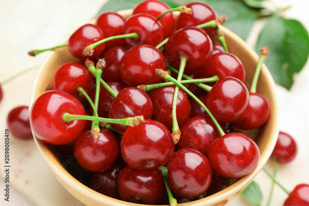 Obraz premium Fresh ripe cherries in bowl and green leaves on table, closeup