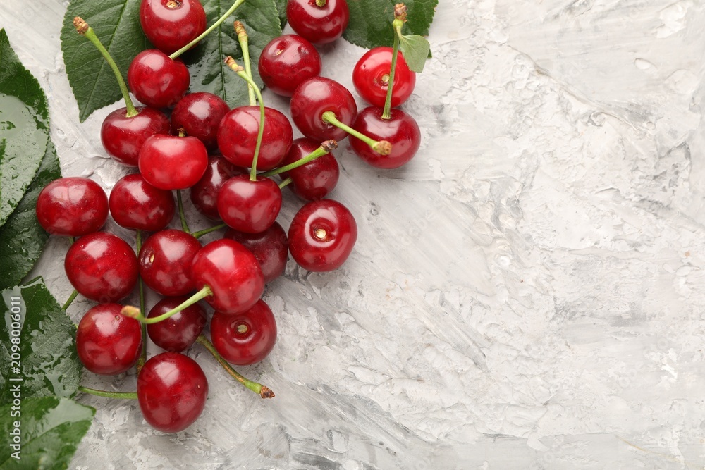 Fototapeta premium Ripe cherries and leaves on light grey table, flat lay. Space for text