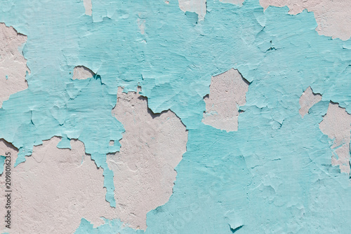 Peeling turquoise paint reveals faded white plaster beneath