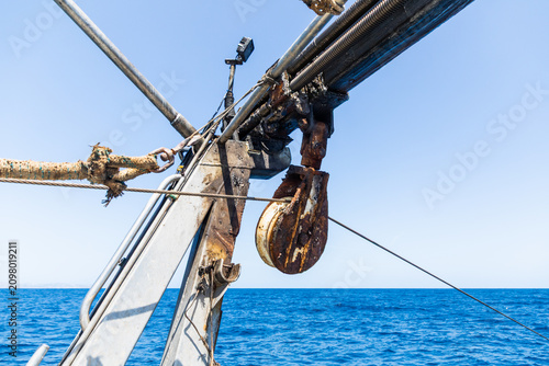 Close-up of rusty ship pulley and rigging above blue sea