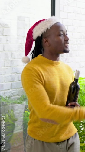 Vertical video: Host opening sliding door mustard man holding bottle Santa-hat entering for holiday