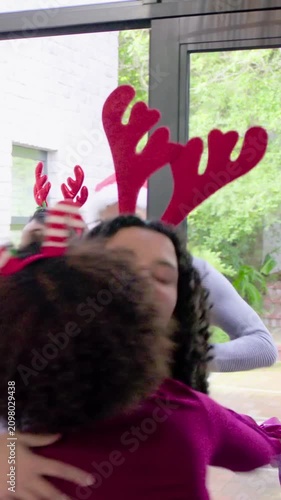 Vertical video: Group handing green gift urging host reaching at home entry hugging with Santa hat