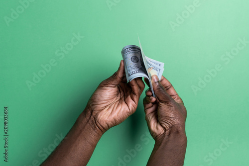 Hands of black man counting US dollar bills on green background