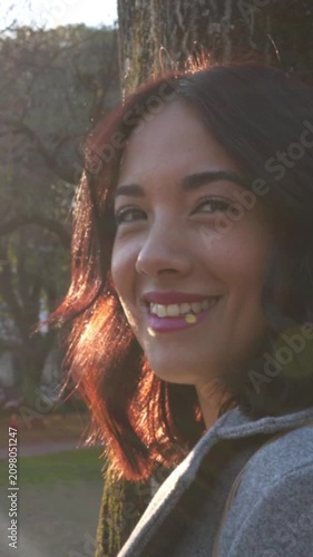 Beautiful hispanic woman smiling at camera in park at sunset. Vertical orientation