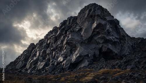 Jagged dark volcanic rock formation rising against a dramatic cloudy sky with golden sunlight breaking through the heavy storm clouds