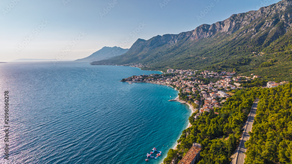 Obraz premium Aerial view of the Adriatic coastline in Croatia with turquoise sea, pine forests, and a coastal town nestled at the foot of the mountains