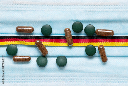 A medical mask with a ribbon in the colors of the German flag and scattered pills on the theme of health, medicine, protection, prevention