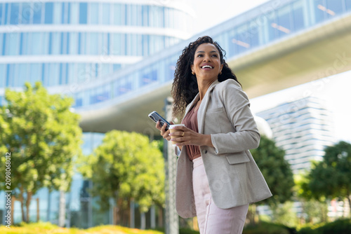 Businesswoman smiling in city holding smartphone and coffee