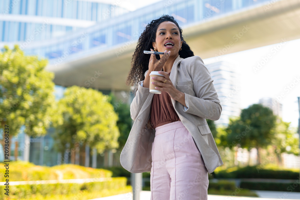 Fototapeta premium Businesswoman recording voice message while walking with coffee