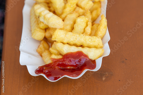 Obraz na płótnie Macro shot of freshly fried, golden crinkle-cut potato chips served in a classic white paper boat with a generous dollop of tomato ketchup on a textured wooden surface