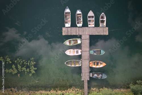 Canvas Print Aerial drone view of a wooden boat dock with several rowing boats moored on a calm lake at dusk, moody atmospheric water reflections