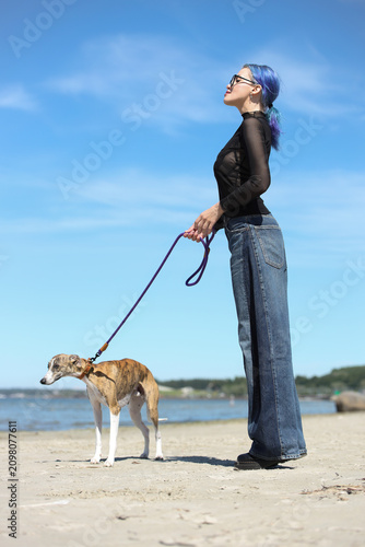 Young woman with blue hair walking dog on beach