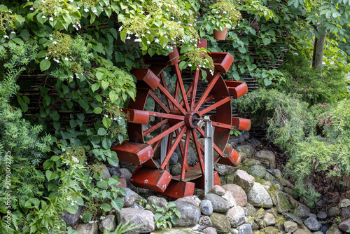 Obraz na plátně Red water wheel among green plants and rocks during daytime