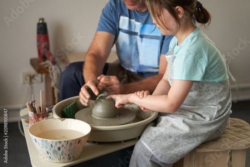 A pottery workshop. A master ceramist teaches a little girl how to stretch a clay object.